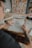 A person with tattoos on their arm is sketching architectural designs on transparent paper at a wooden table. Nearby, there are notebooks filled with other sketches, a vase with white flowers, and a set of colored markers. In the background, a colorful abstract painting is visible.