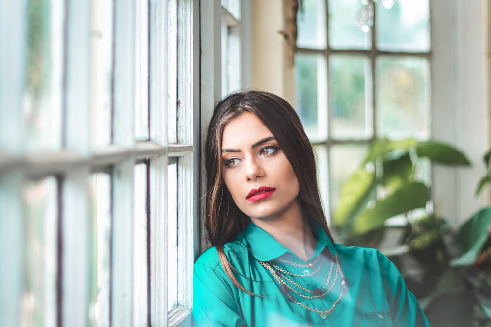 a woman leaning against a window with a green shirt on