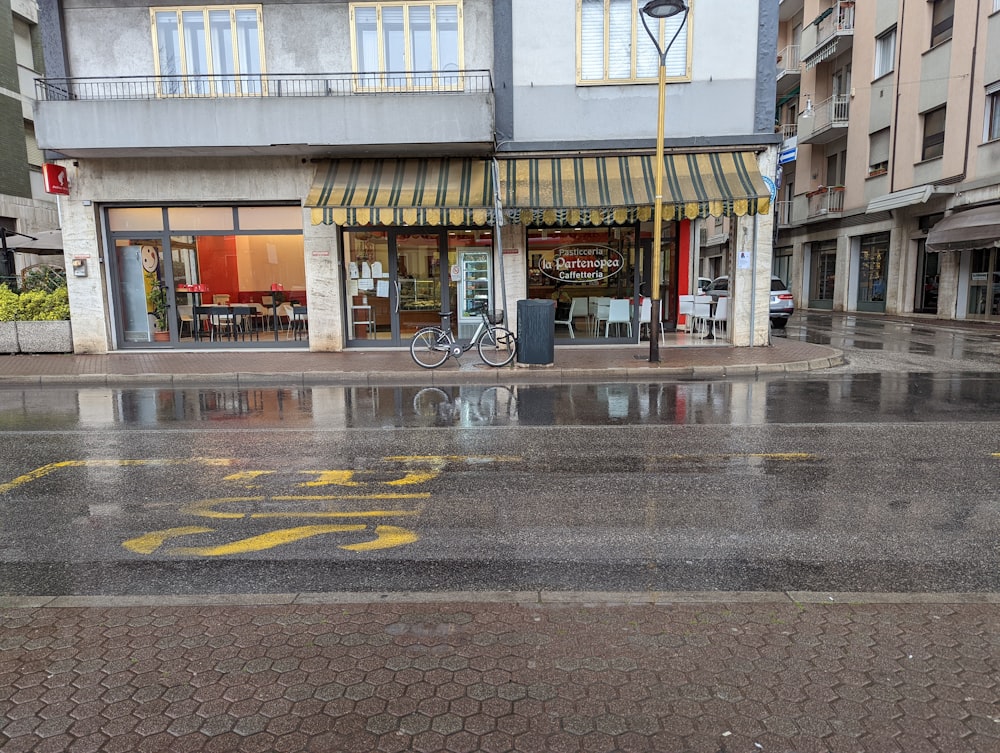 a wet street in front of a building with a bicycle parked in front of it