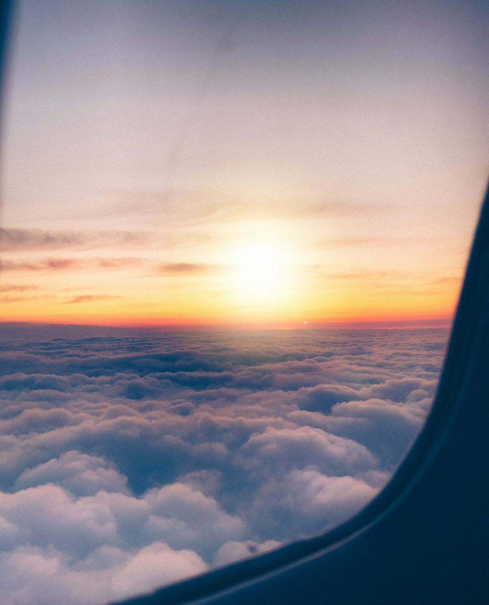 the sun is setting over the clouds as seen from an airplane window