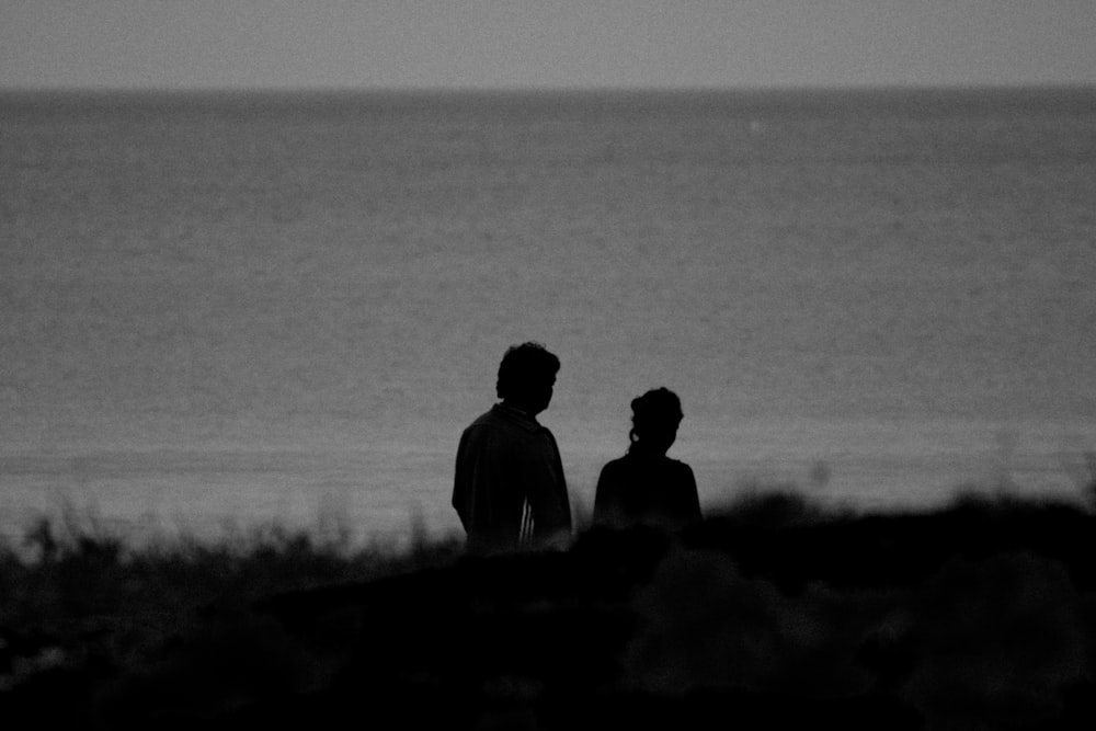 two people standing in front of a body of water