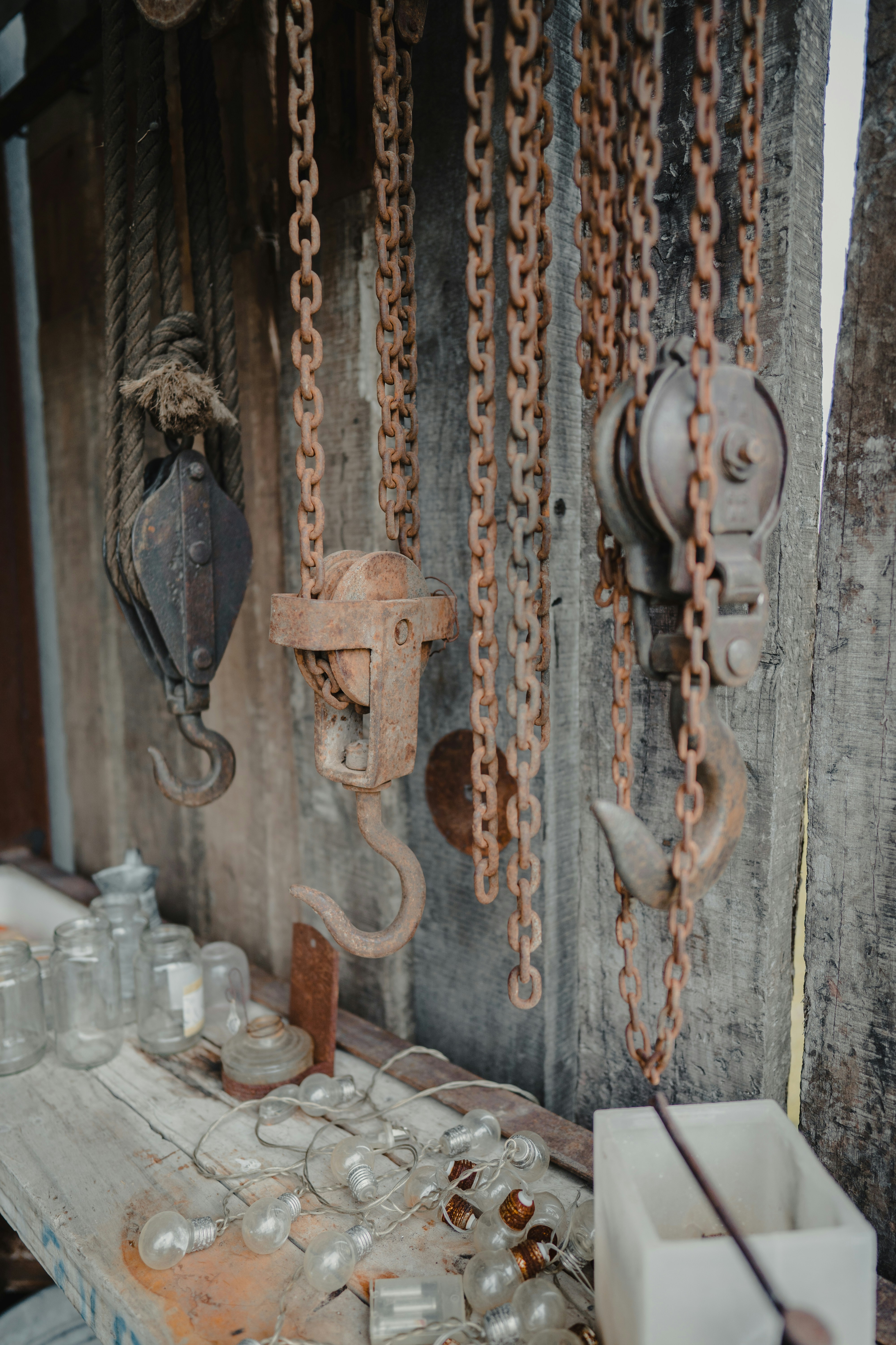 Outdoor workbench with old rusty chains and hooks hanging over glass jars, lamps and candles.