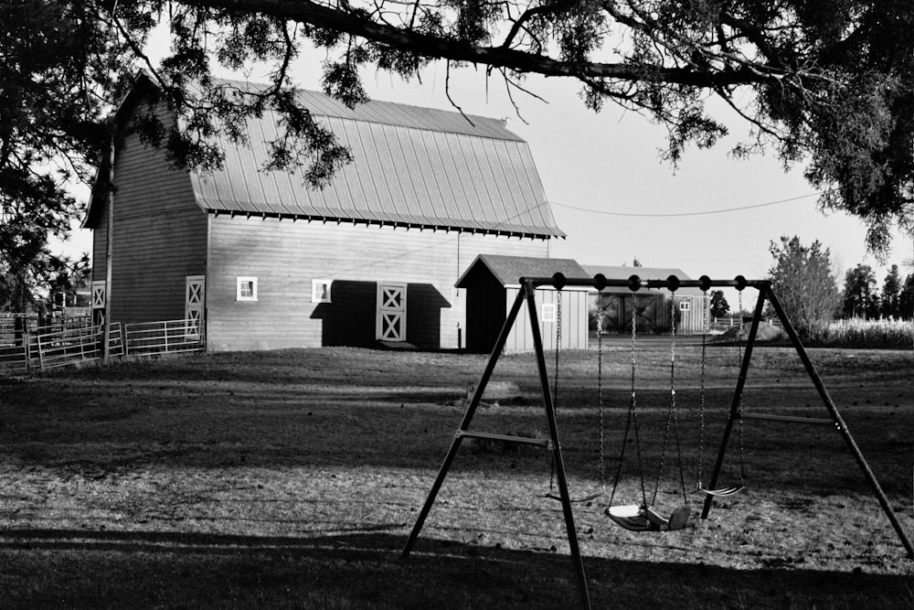 a black and white photo of a swing set in front of a barn