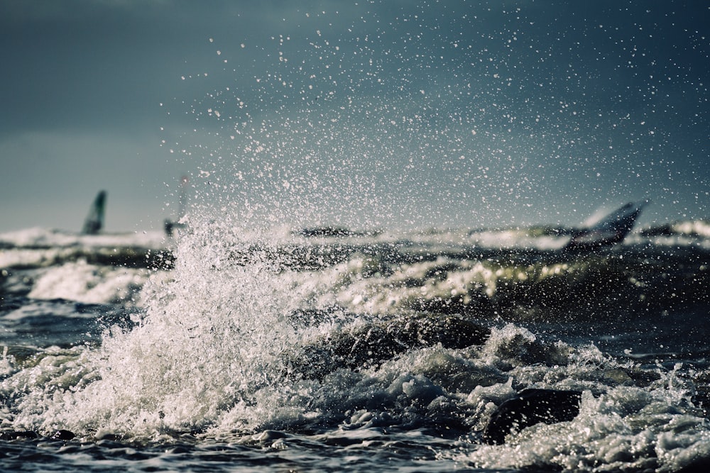 a wave crashing into the ocean with a boat in the background