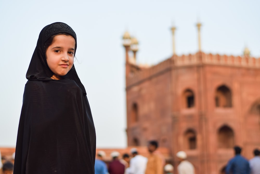 a young girl in a black shawl standing in front of a building