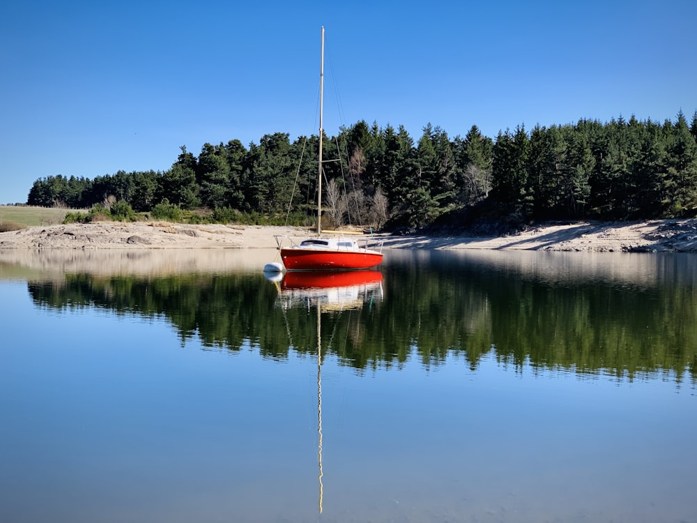 a red boat floating on top of a lake next to a forest