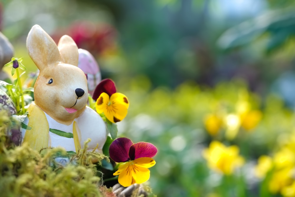 a close up of a toy rabbit in a field of flowers