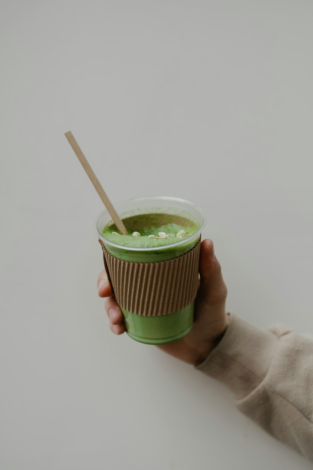 a hand holding a cup of green liquid