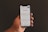 A hand is holding a smartphone displaying the Google search page, which shows trending search topics. The phone screen is bright against a dark background.