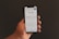 A hand is holding a smartphone displaying the Google search page, which shows trending search topics. The phone screen is bright against a dark background.