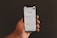 A hand is holding a smartphone displaying the Google search page, which shows trending search topics. The phone screen is bright against a dark background.