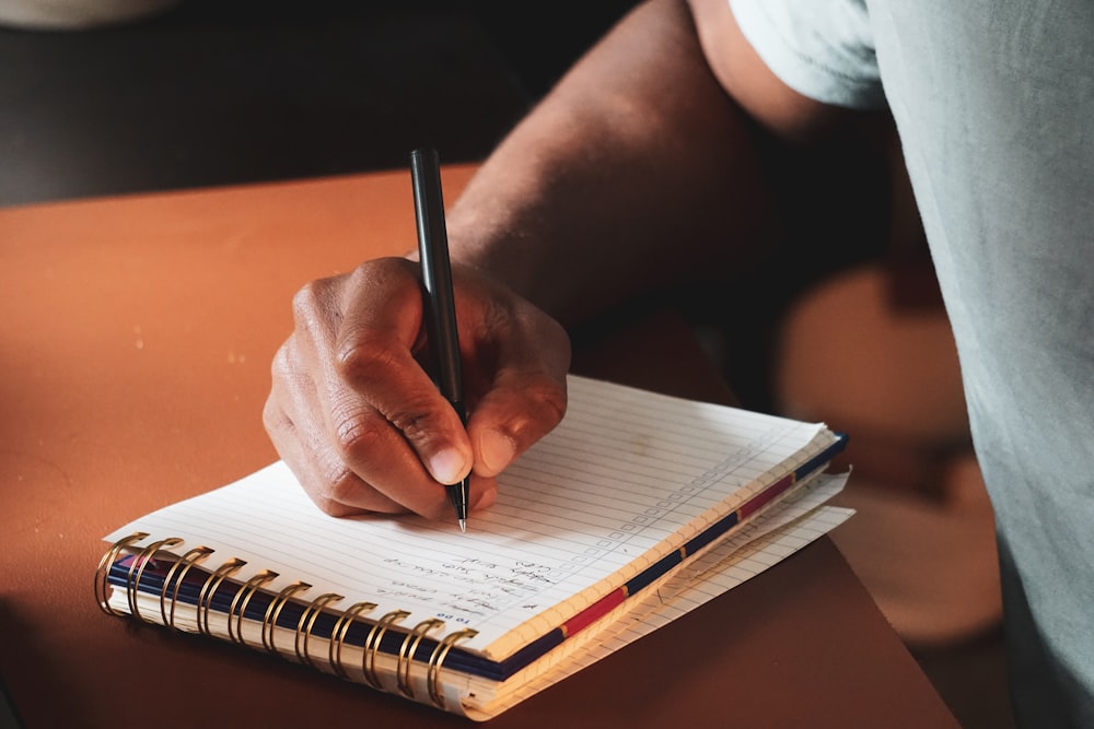 a person writing on a notebook with a pen