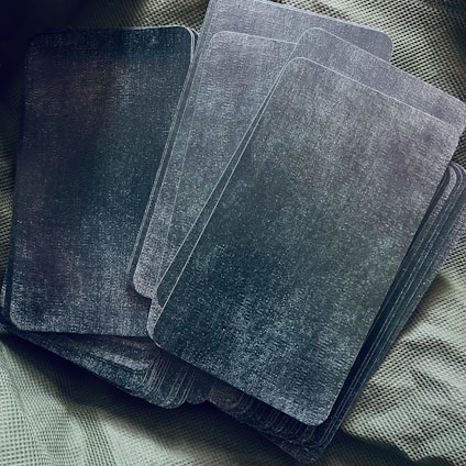A group of rectangular cards with a dark, textured surface arranged on a textured fabric background. The cards appear to be piled casually, with some overlapping.