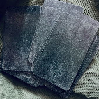 A group of rectangular cards with a dark, textured surface arranged on a textured fabric background. The cards appear to be piled casually, with some overlapping.
