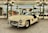 A vintage white Mercedes-Benz sports car is displayed in an elegant showroom. The car features iconic gull-wing doors that are open, showcasing its luxurious design. The background has ornate green lamp posts and mirrored walls reflecting other classic cars and visitors, creating an atmosphere of sophistication and nostalgia.