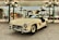 A vintage white Mercedes-Benz sports car is displayed in an elegant showroom. The car features iconic gull-wing doors that are open, showcasing its luxurious design. The background has ornate green lamp posts and mirrored walls reflecting other classic cars and visitors, creating an atmosphere of sophistication and nostalgia.