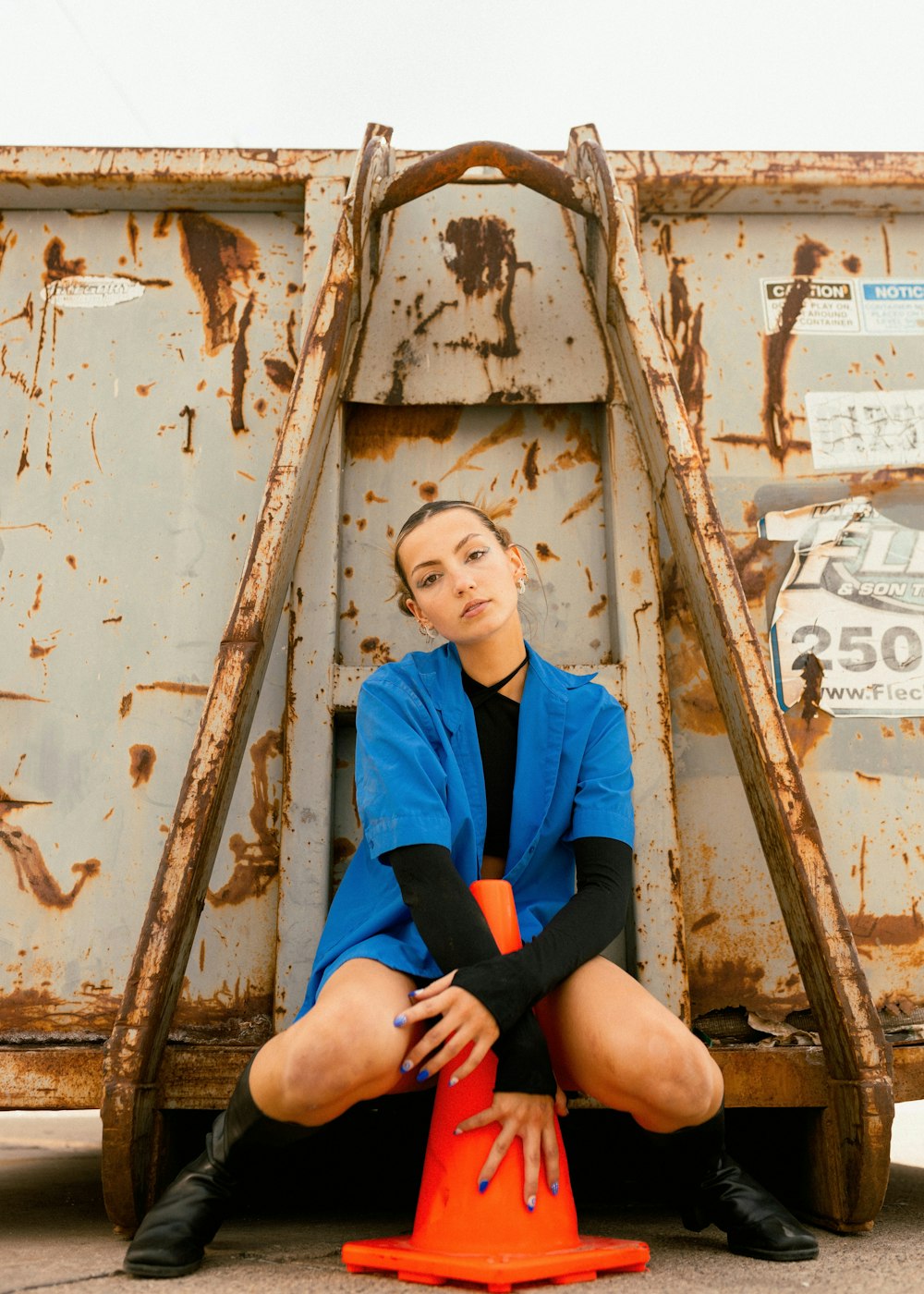 a woman sitting on the ground next to a dumpster