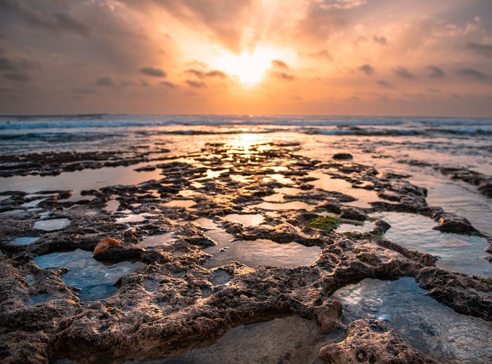 the sun is setting over a rocky beach