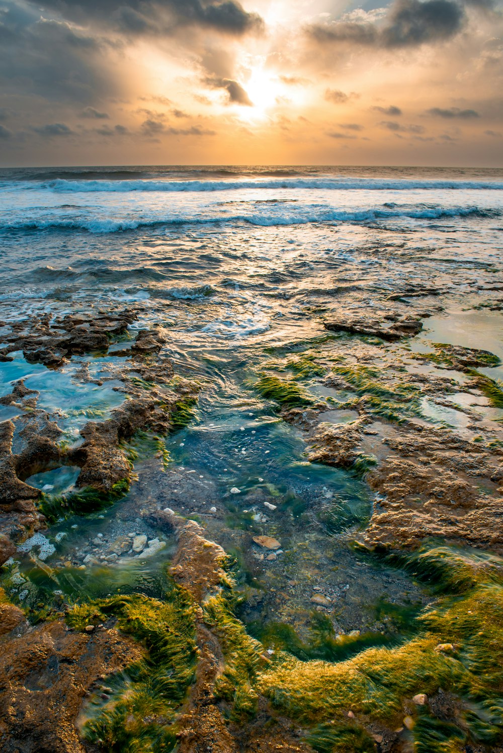 o sol está se pondo sobre o oceano e as rochas