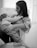 A tender moment between a woman and a young child as they cuddle in a comfortable chair. The woman holds the child close to her chest, and both appear to be relaxed and at peace. The scene is intimate and conveys a sense of warmth and connection.