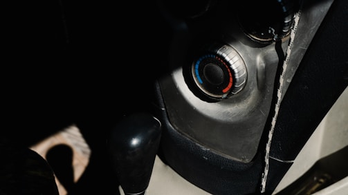 A close-up view of a car's interior focusing on the temperature control dial with blue and red markings. The image also features part of the gear shift lever and console, with a mix of shadows and highlights from natural lighting.