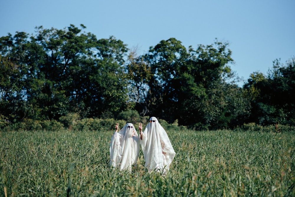 two women dressed in white walking through a field