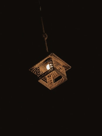 A hanging woven lamp illuminates the darkness, casting a warm glow. The lamp features a geometric pattern made from natural materials, possibly bamboo or rattan, and is suspended by a sturdy cord.