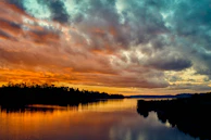 A cinematic wide shot of a sunset over a calm river, with vibrant colors reflecting on the water.