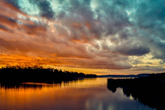 A cinematic wide shot of a sunset over a calm river, with vibrant colors reflecting on the water.