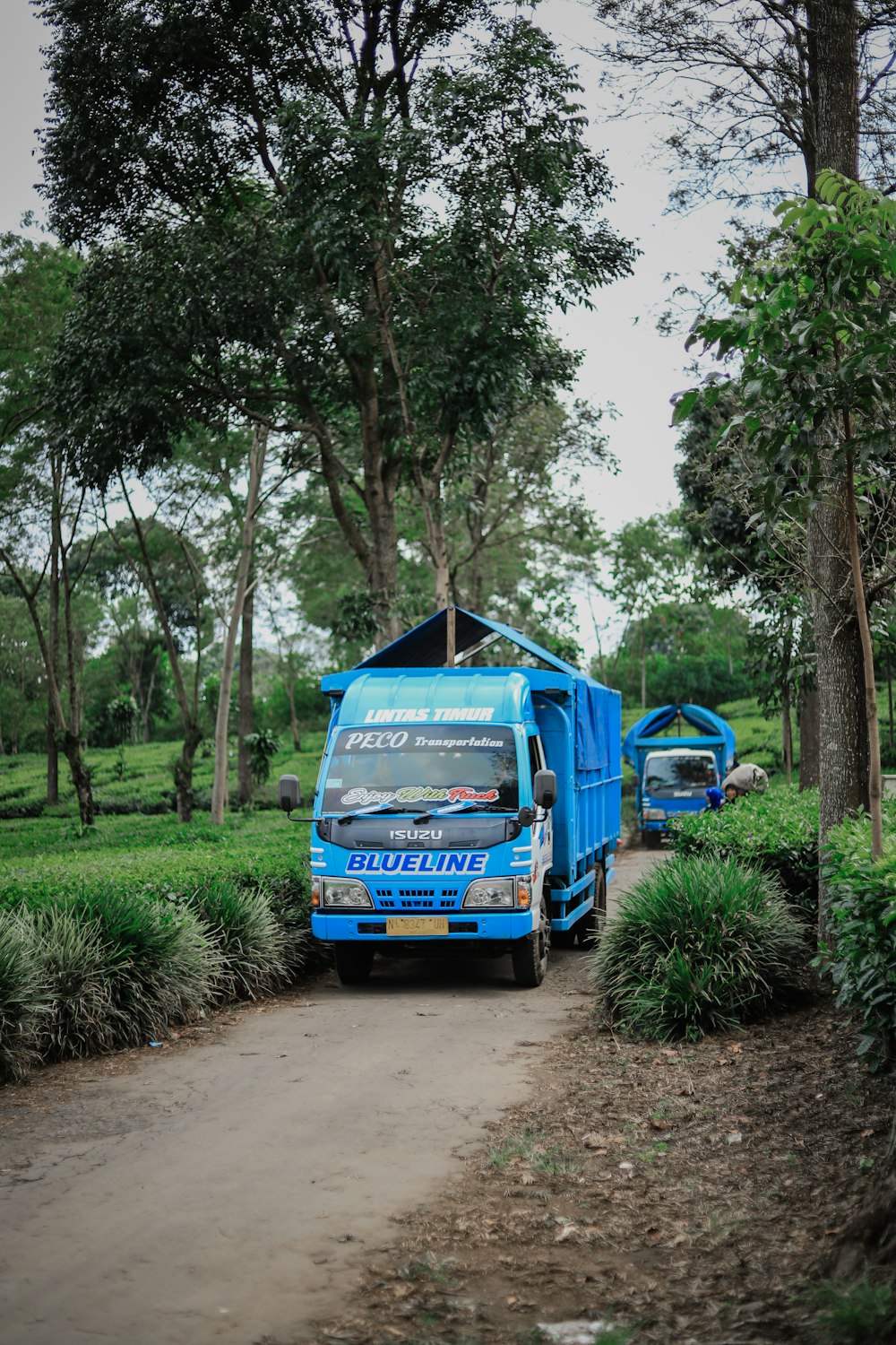 a blue garbage truck parked on a dirt road