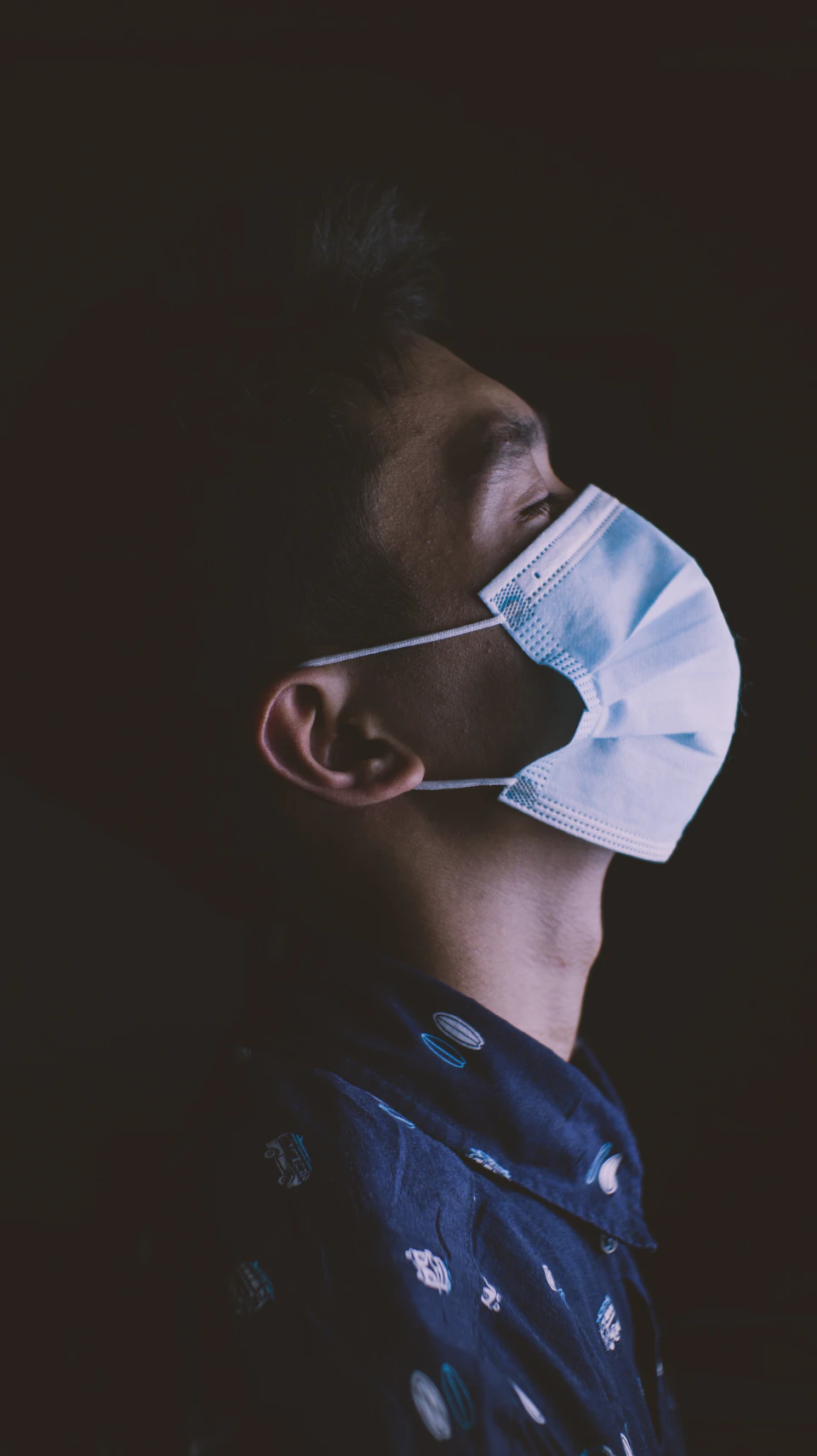 Person tilts head back, wearing blue and white polka dot shirt and face mask