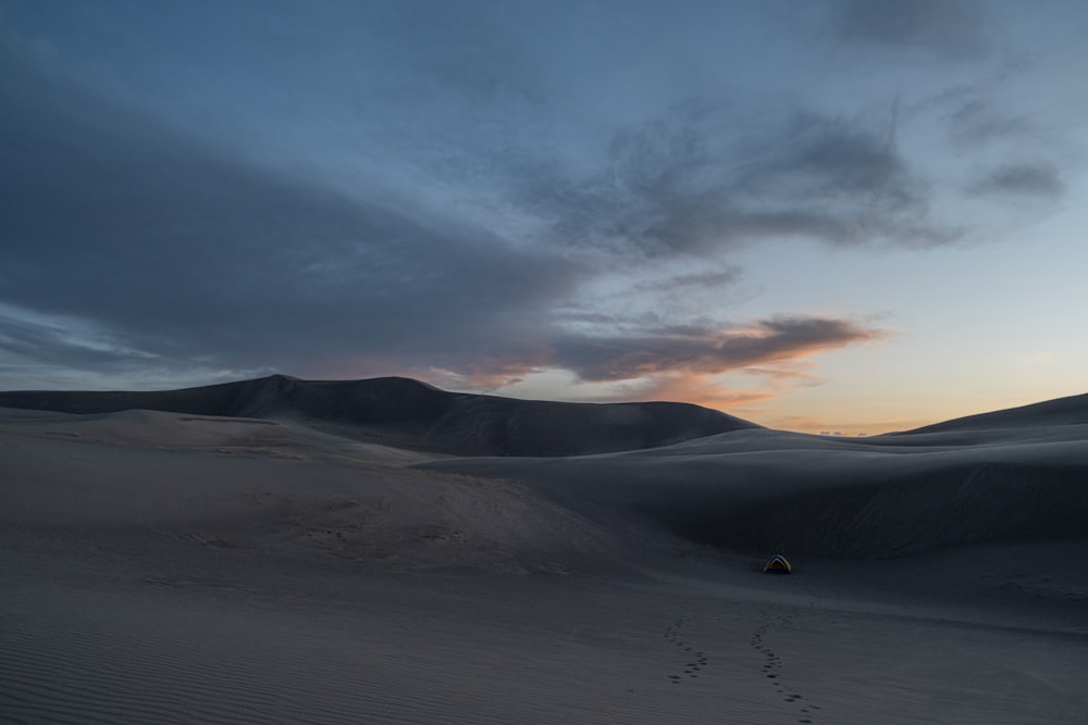 a person walking across a sandy field at sunset