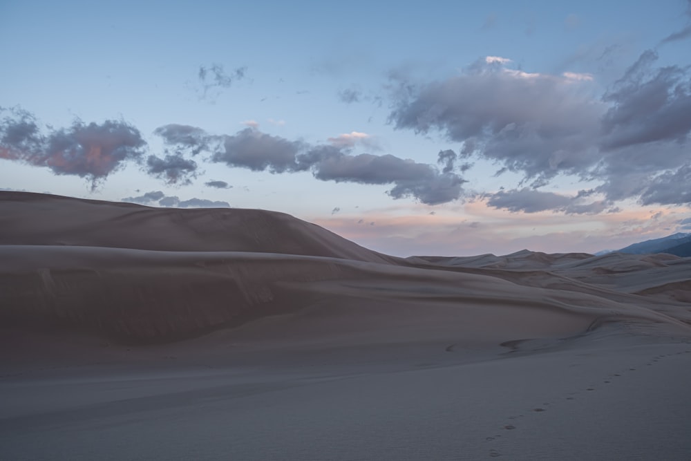 a desert with sand dunes and clouds in the sky