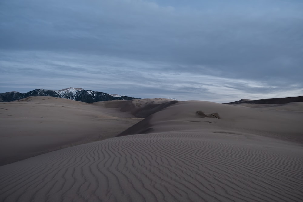 sand dunes with mountains in the distance under a cloudy sky