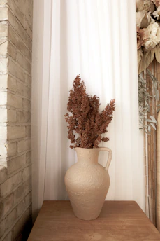 Close-up of a textured ceramic vase in soft earth tones with dried flowers inside.