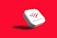 A white, rounded square object with the Bank of America logo displayed prominently. The logo features stylized red and blue stripes above the text 'BANK OF AMERICA'. The object casts a shadow on a vibrant red background, giving the impression that it is floating.