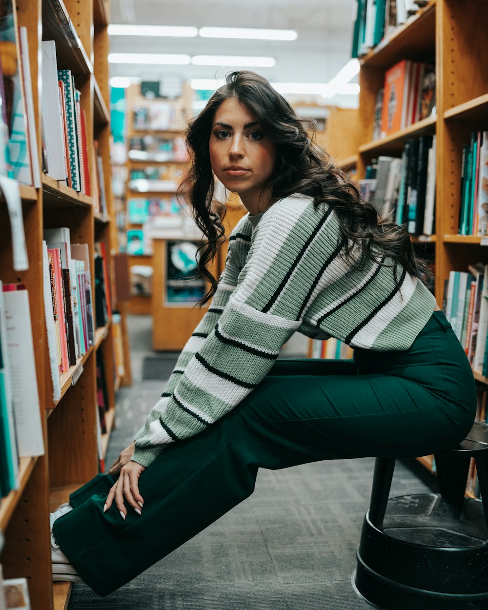 a woman sitting on a stool in a library