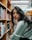A stylish woman browsing through a library filled with books.