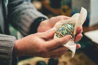 Close-up of a hand delicately applying wax to a traditional Sorbian Easter egg in a cozy workshop.