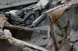 A scene of collapsed concrete structures with visible reinforcement steel bars and extensive rust. Debris and broken concrete slabs are scattered around, indicating a significant structural failure.
