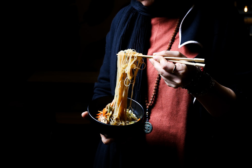 a person holding a bowl of noodles with chopsticks