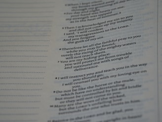 A close-up view of a book or document showing a section of text printed in a serif font. The text contains numbered lines, potentially verses or key points, and is formatted in a column layout. The background is a light color, typical of paper. The text on the left shows dotted lines, possibly for notes or annotations.