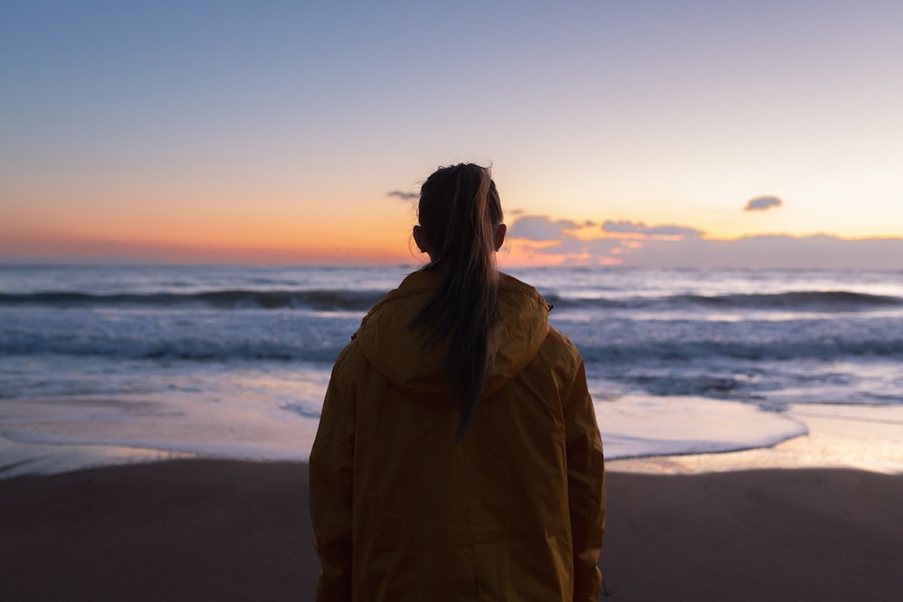 a woman standing on the beach watching the sunset