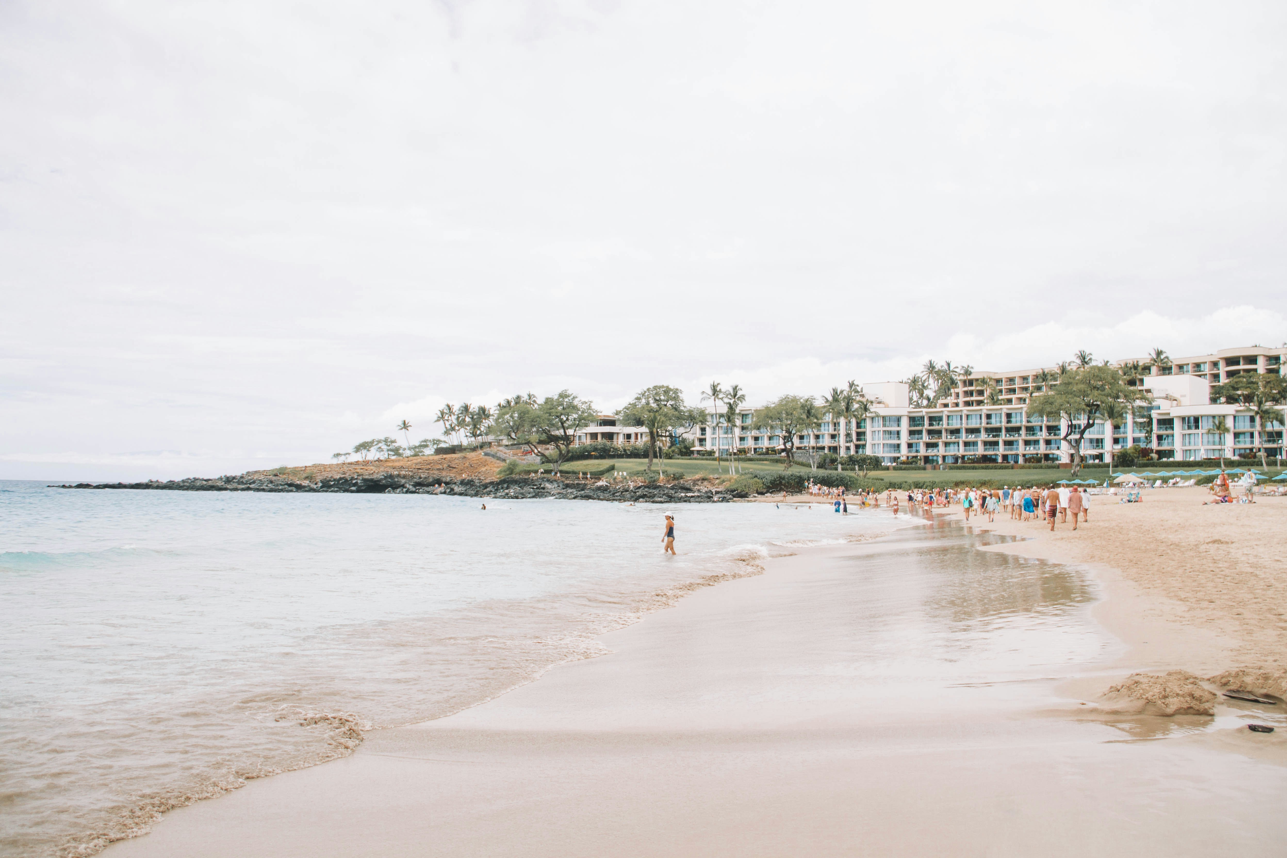 a beach with people walking on it and buildings in the background, 