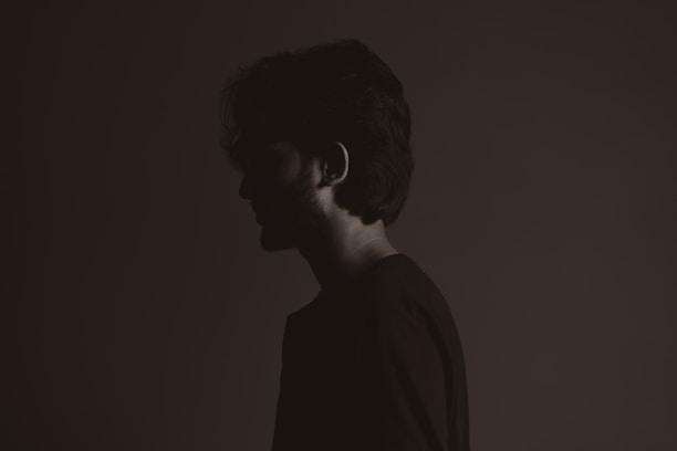 A moody portrait of a person silhouetted against a dark, textured backdrop with subtle highlights.