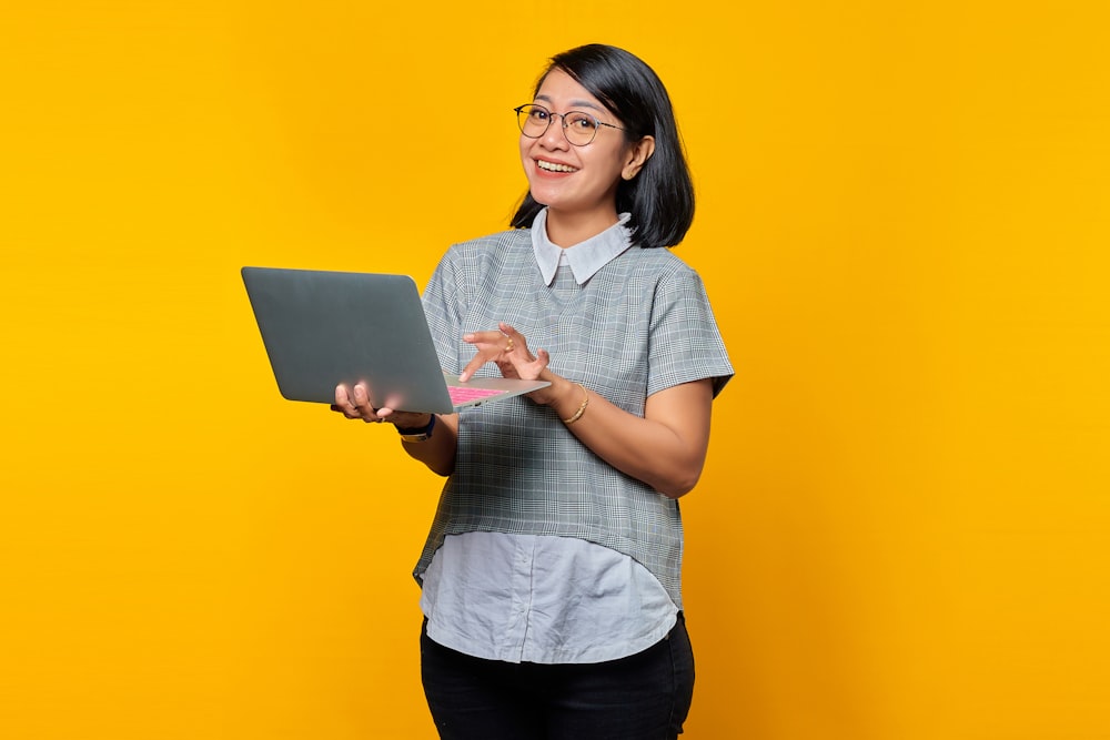 a woman holding a laptop computer on a yellow background