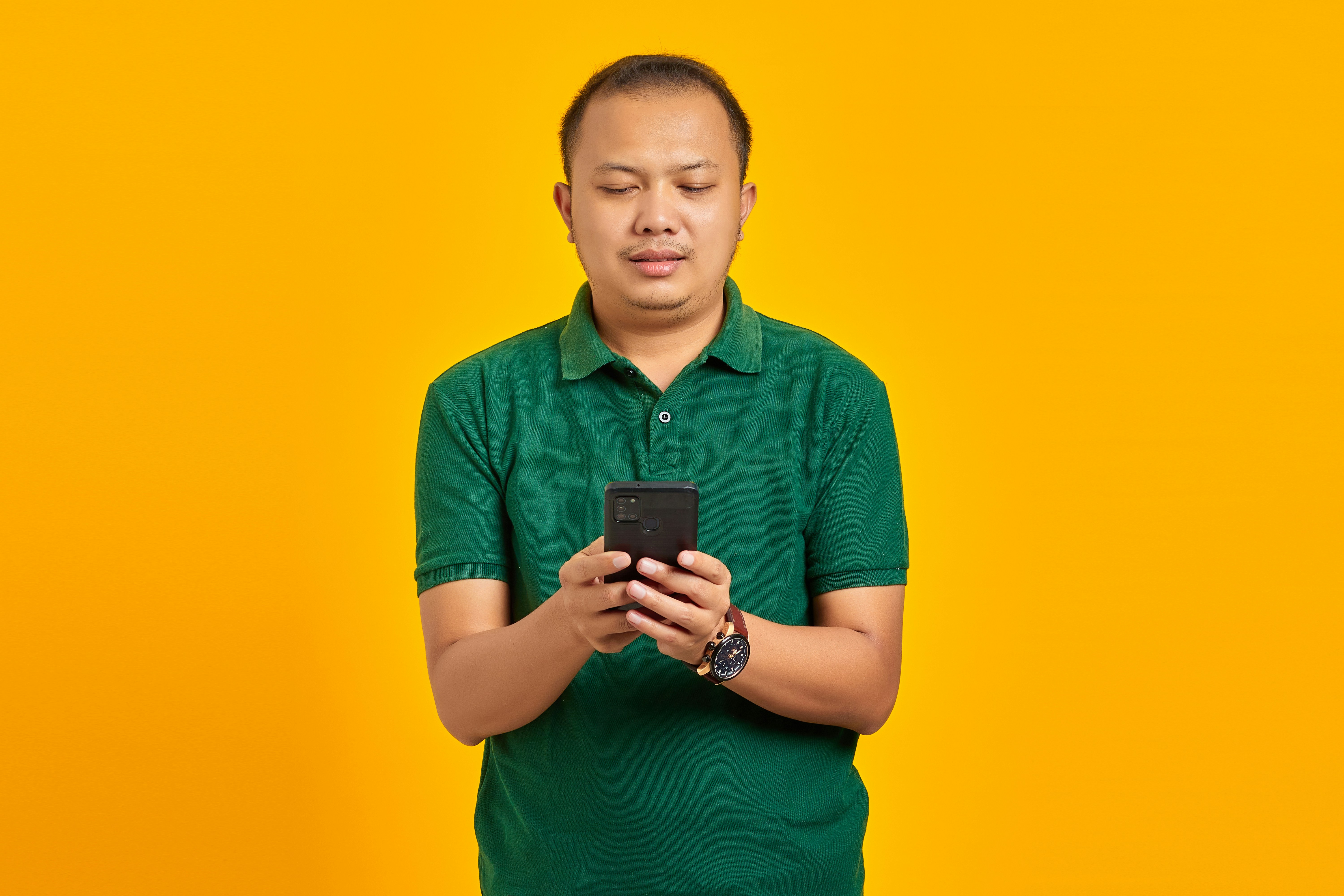 Portrait of cheerful young Asian man using a mobile phone on yellow background