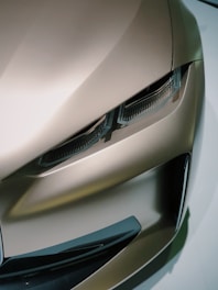 A close-up view of a sleek, modern car headlight and a portion of the car's body, showcasing a streamlined design with sharp angles and smooth surfaces. The image highlights the car's detailed workmanship and futuristic aesthetics.