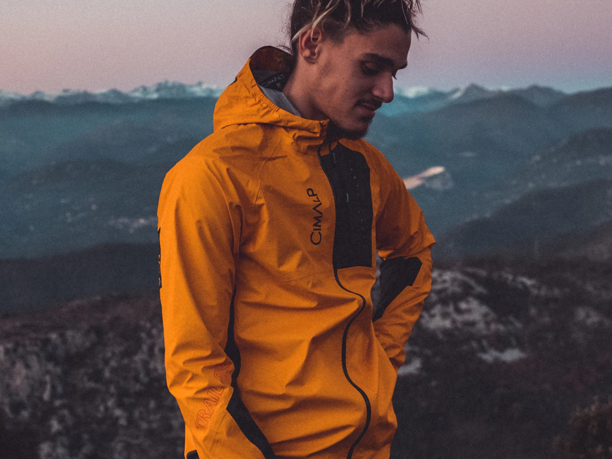 Hiker in a yellow technical shell jacket standing on a mountain ridge