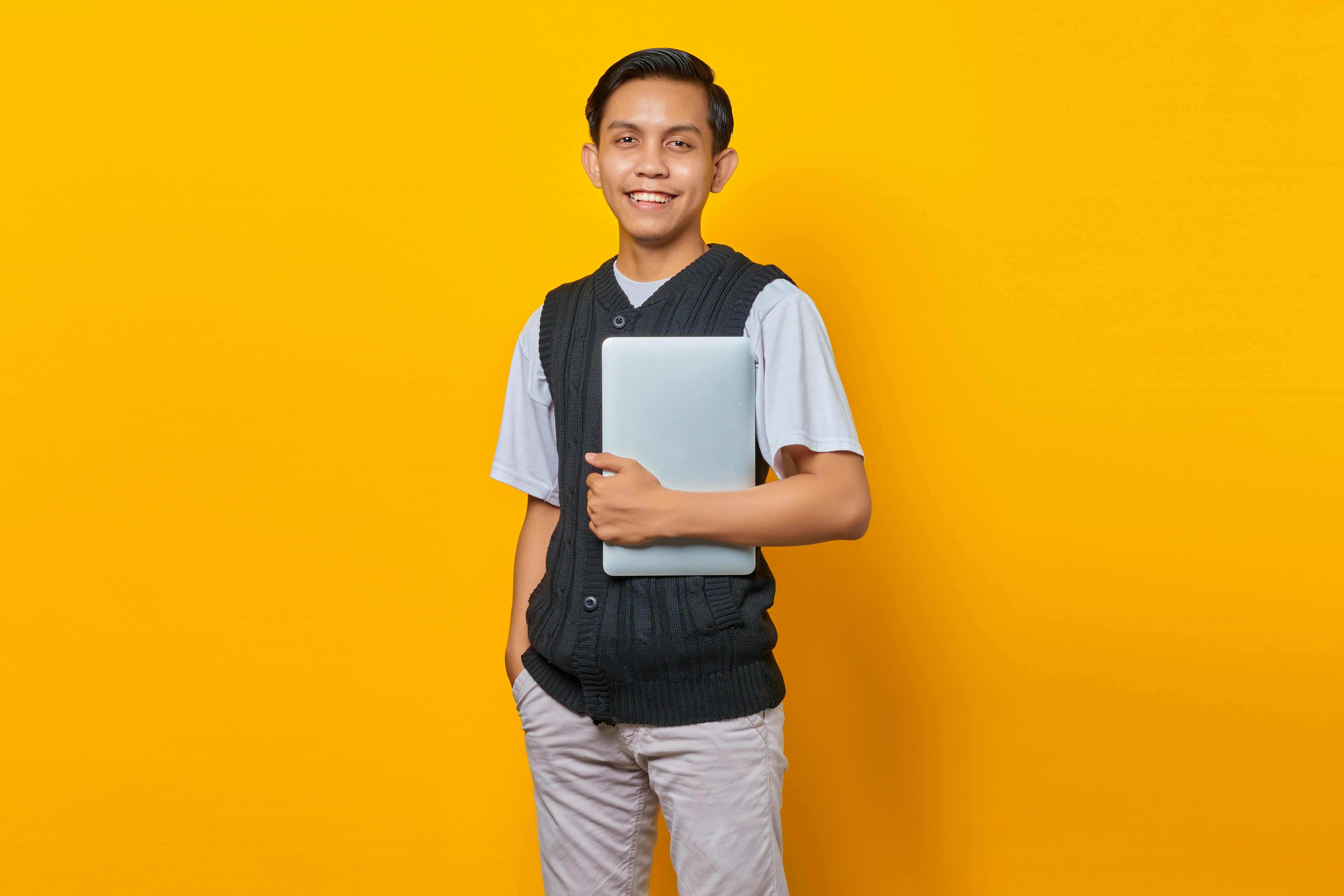 Portrait of smiling Asian man bring laptop over yellow background